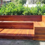 Custom-designed wooden benches integrated into a multi-level deck in a Sydney outdoor space, surrounded by lush green shrubs, showcasing expert craftsmanship from custom designed benches service.