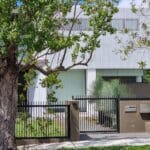 Modern black metal fence with a concrete pillar in front of a contemporary house in Sydney, surrounded by lush greenery and a large tree, highlighting a professional fence installation service.