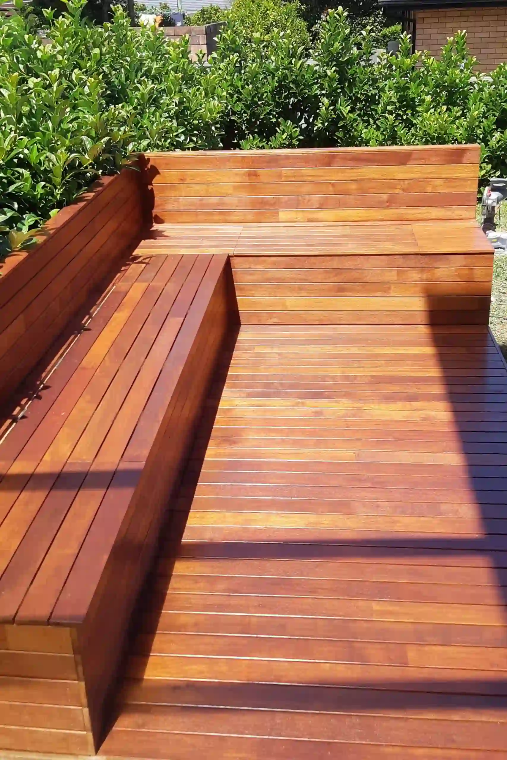 Custom wooden L-shaped bench on a deck by Arianiya Landscapes in Sydney, surrounded by greenery.