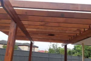 Custom timber pergola with a slatted roof in a Sydney backyard, built by Ariyania Landscapes, featuring a dark fence and lush greenery, showcasing expert pergola construction and backyard pergola design services.