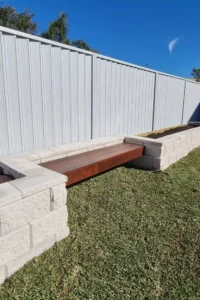 Arianiya Landscapes' custom wooden bench in a Sydney garden, set against a brick wall and lush plants