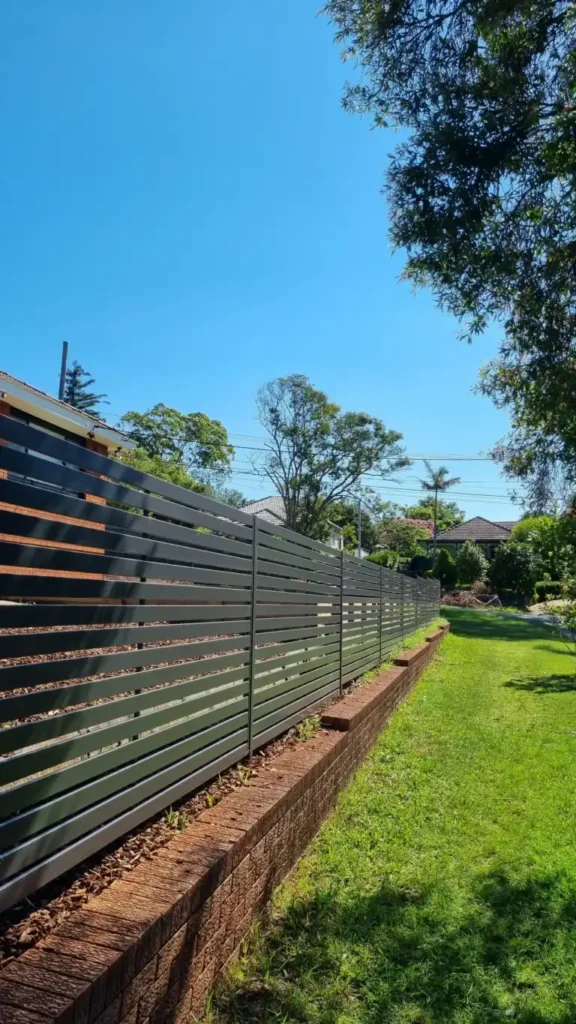 Epping landscaping in Epping, Sydney, by Arianya, with a black slatted fence and brick wall on a green lawn, crafted for low-maintenance style.