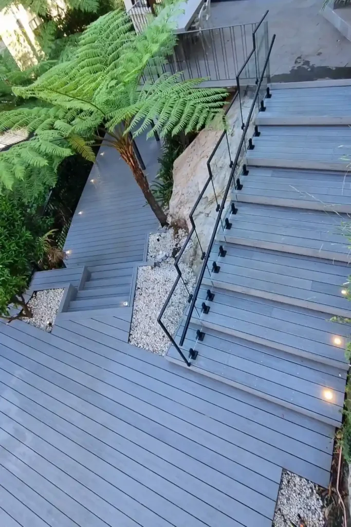 Stylish Aussie deck ideas by Arianya, featuring grey timber, glass railings and soft deck lighting at night.