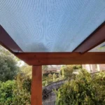 Timber pergola with a transparent roof by Ariyania Landscapes in a Sydney garden, surrounded by lush greenery and a wooden fence, showcasing expert pergola construction and outdoor pergola design services.