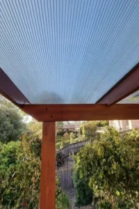 Timber pergola with a transparent roof by Ariyania Landscapes in a Sydney garden, surrounded by lush greenery and a wooden fence, showcasing expert pergola construction and outdoor pergola design services.