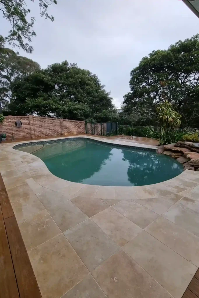 Elegant pool paving in Sydney by Ariyania Landscapes for a big backyard surrounded by tall trees.