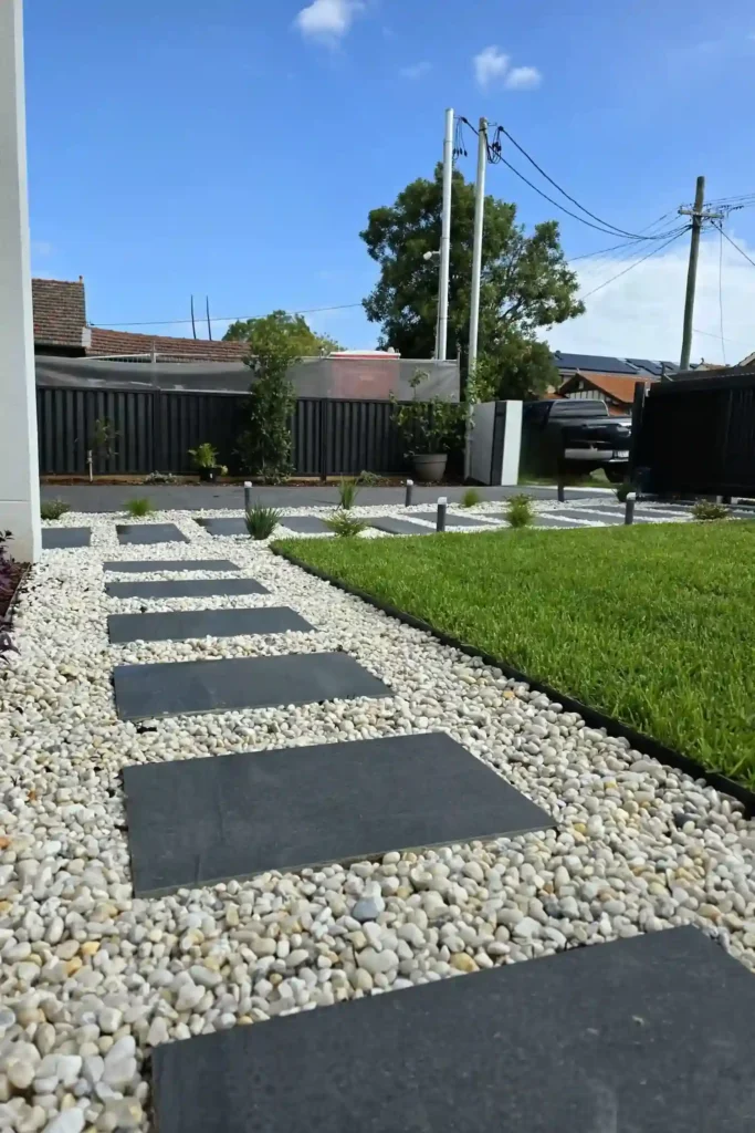 Modern paving design for a Sydney driveway and garden path, featuring dark pavers set in white gravel and complemented by a Colorbond fence.
