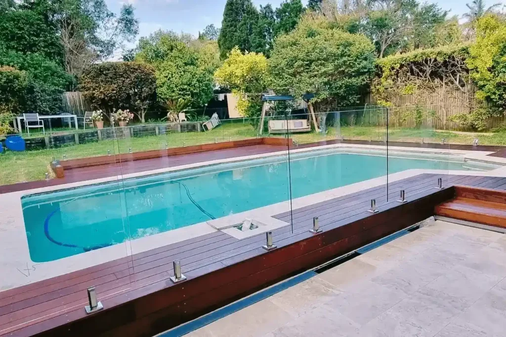 Aussie deck ideas: stunning poolside deck with glass fencing and wooden surround, nestled in a lush Newcastle backyard.