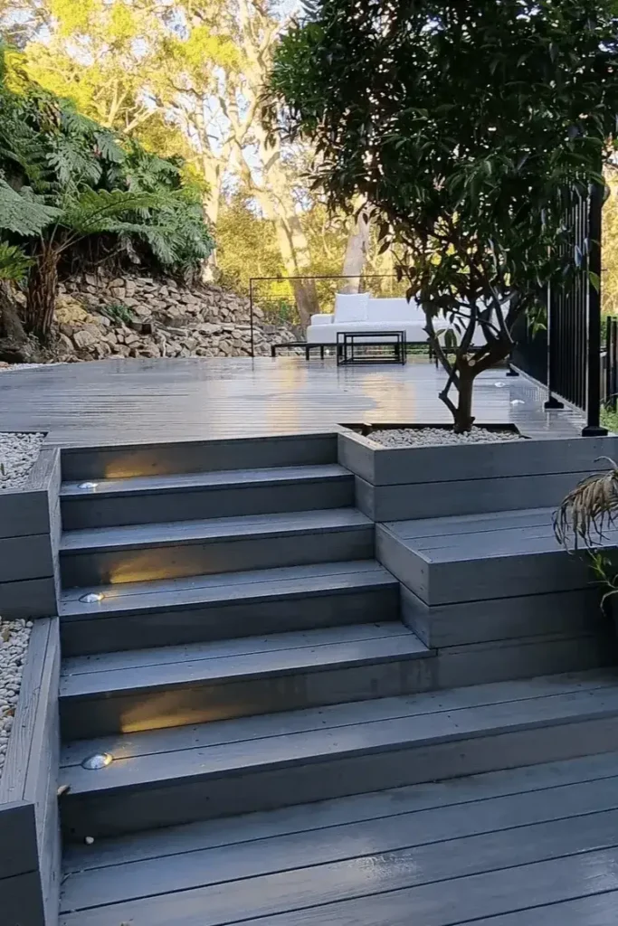 Aussie deck ideas: sleek grey deck with lit steps, plants, and a comfy lounge area in a lush Sydney backyard.