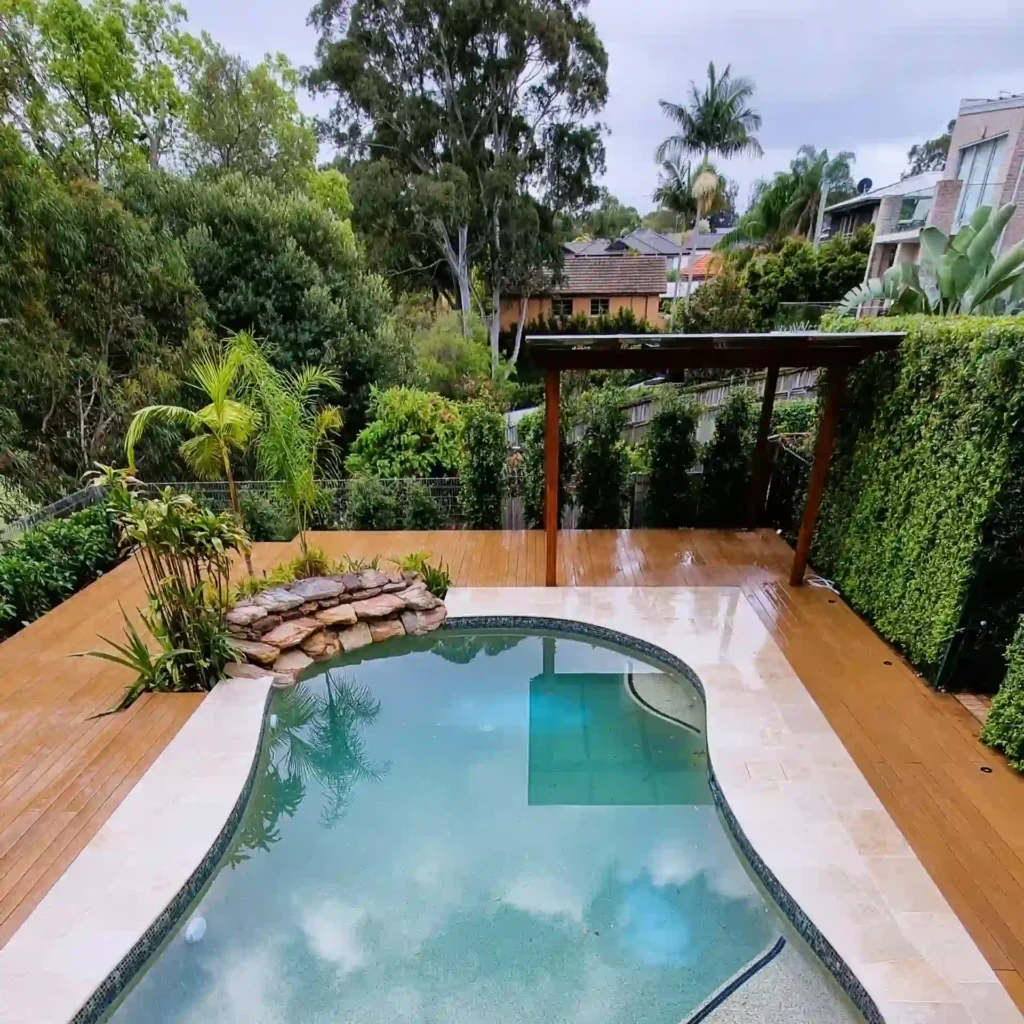 Stylish deck ideas: wooden deck with a pool, pergola, and lush greenery, overlooking a scenic backyard on a rainy day.