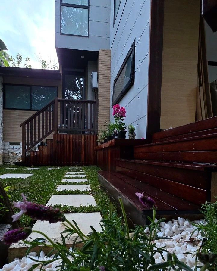 Garden design showcasing pink and white blooms with artificial turf in paving joints, elegant dark timber deck stairs, and timber retaining wall surrounded by potted flowers.
